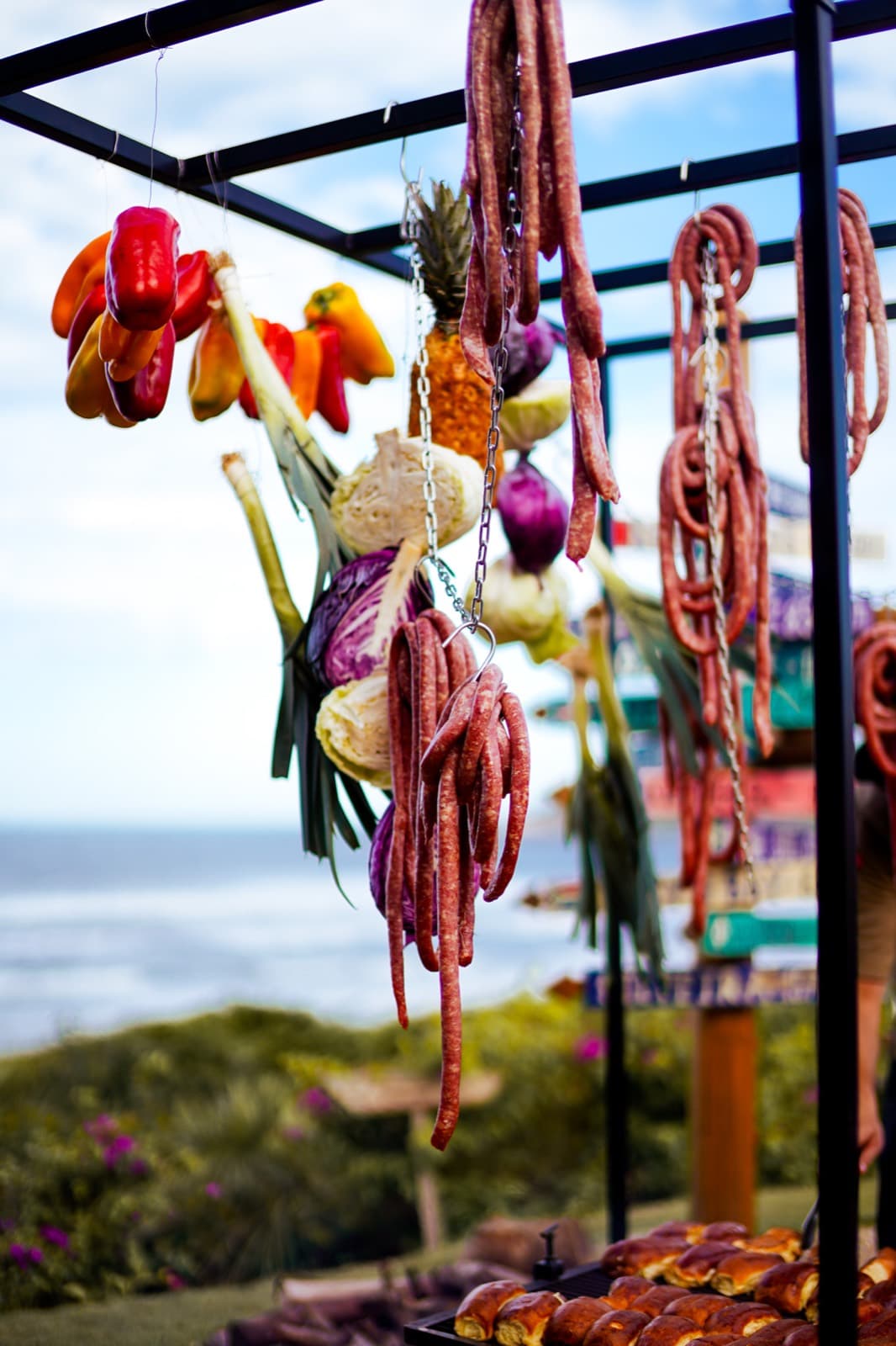 Legumes e frutos do mar coloridos pendurados na estrutura da parrilla, o mar ao fundo