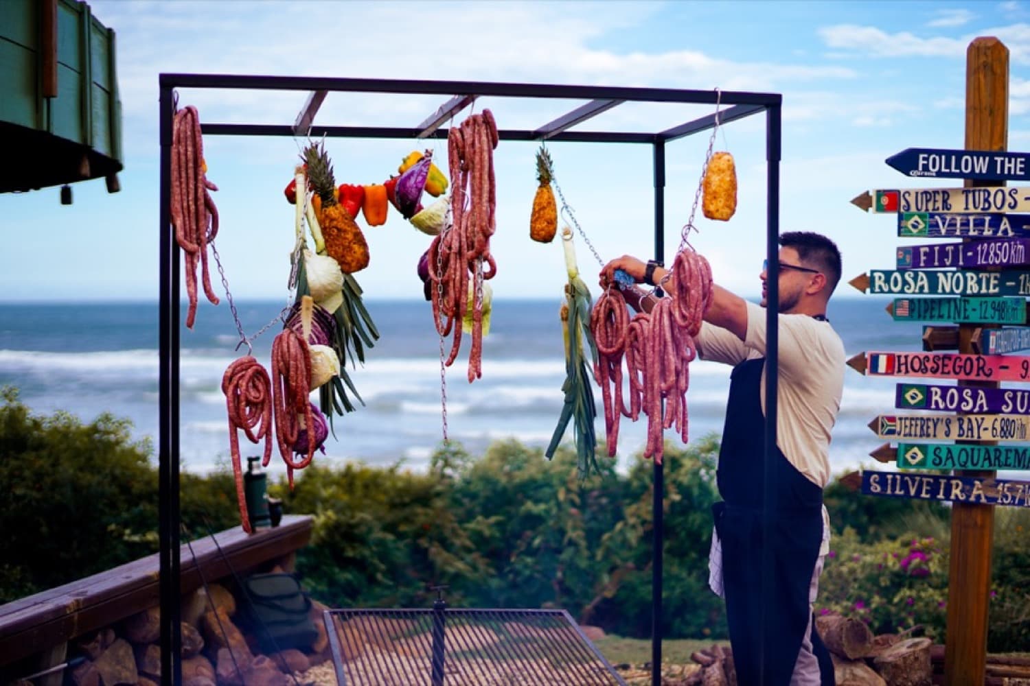 Chef João montando a parrilla à beira-mar, com o mar ao fundo